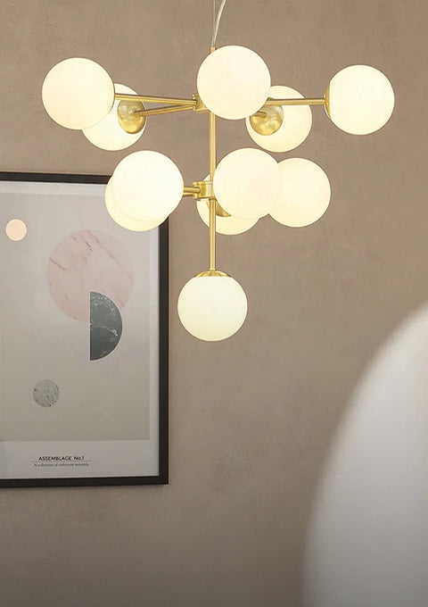 Gold multi globe chandelier with white glass shades hanging in front of a framed abstract print
