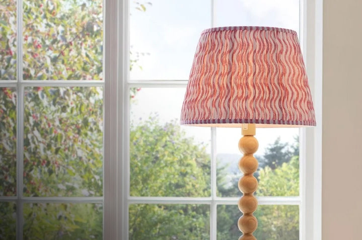 Table lamp with a wooden ball base and a red wavy patterned fabric shade in front of a window