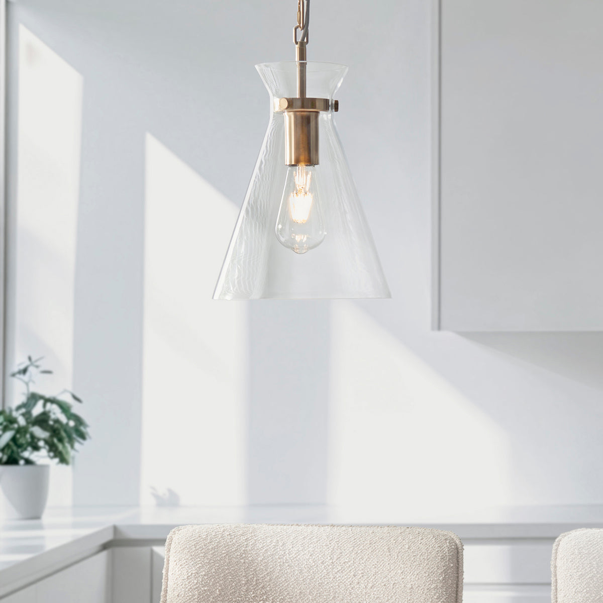 A modern pendant light with a clear glass shade and brass accents hangs in a bright, minimalist room.
