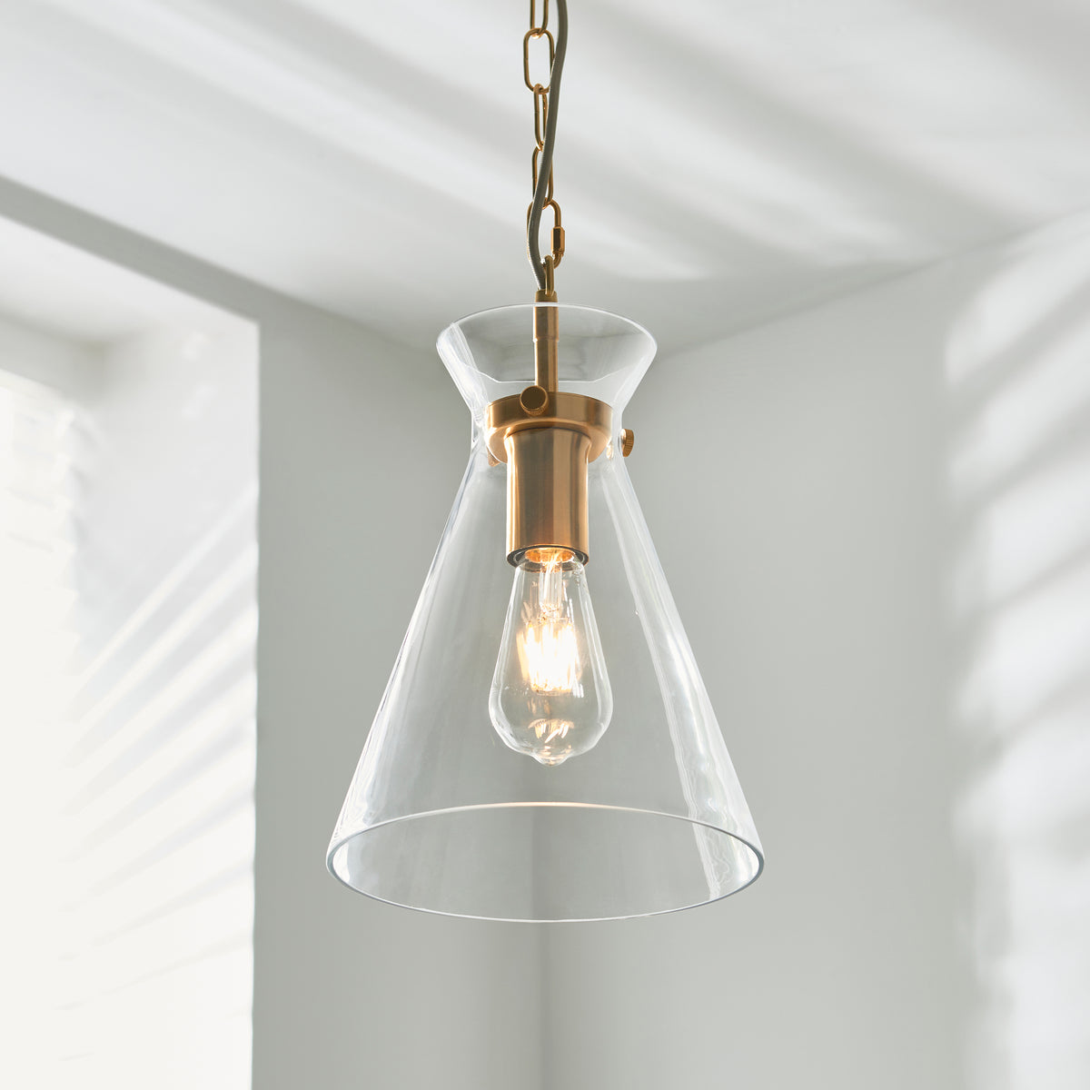 A clear glass pendant light with a brass fixture and an exposed Edison bulb hangs from a ceiling.