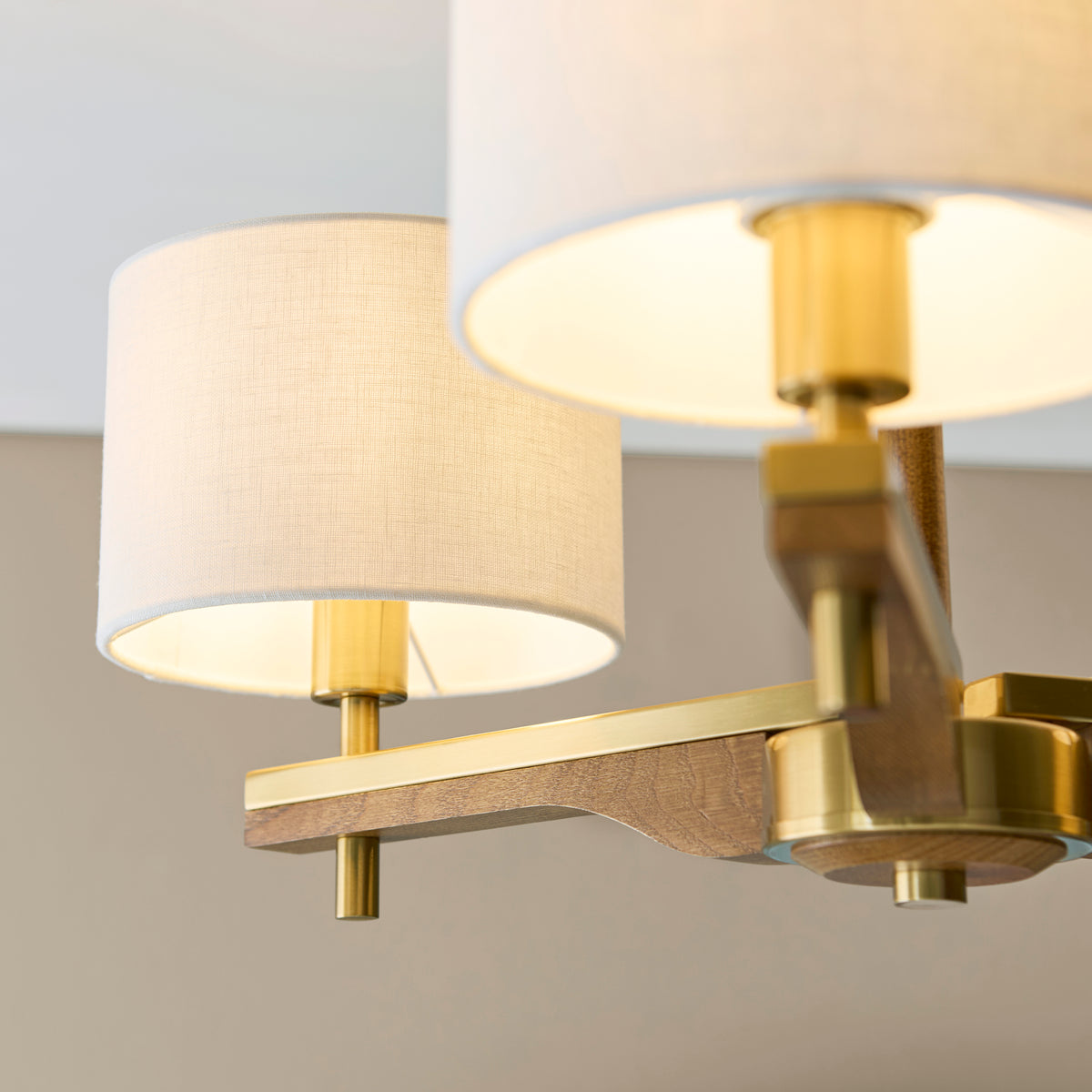 Close-up of a modern chandelier with two fabric shades, brass accents, and a wooden frame.