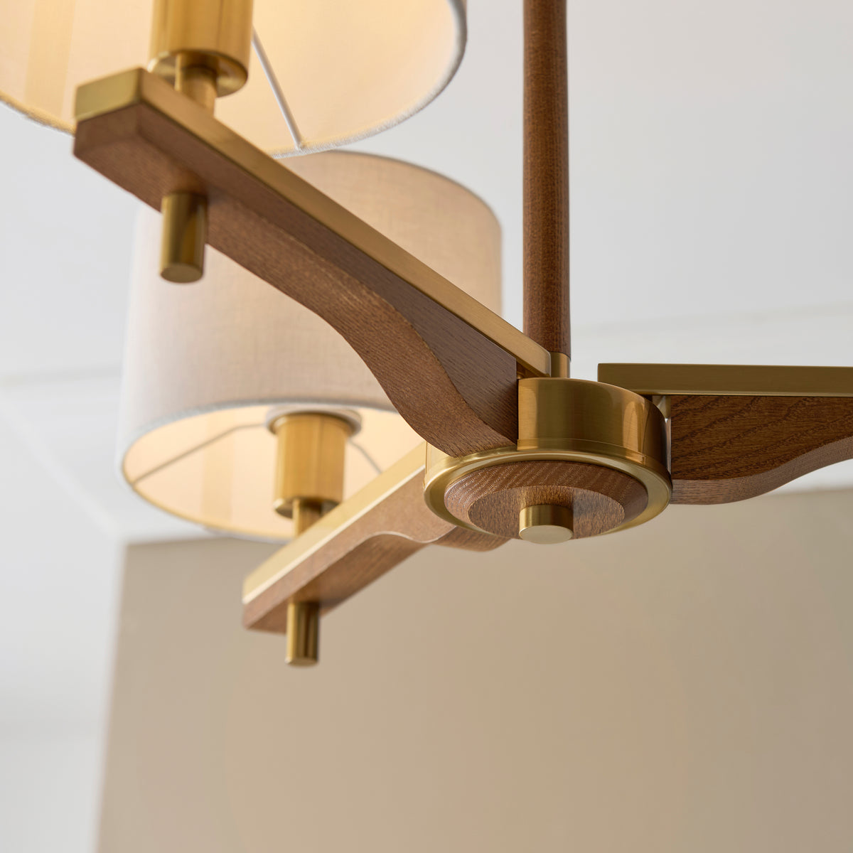 Close-up of a modern chandelier with wooden arms, brass accents, and fabric shades.