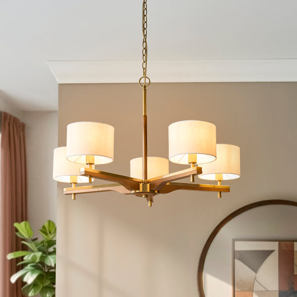 A modern chandelier with five white fabric shades and a wooden and brass frame hangs from the ceiling.