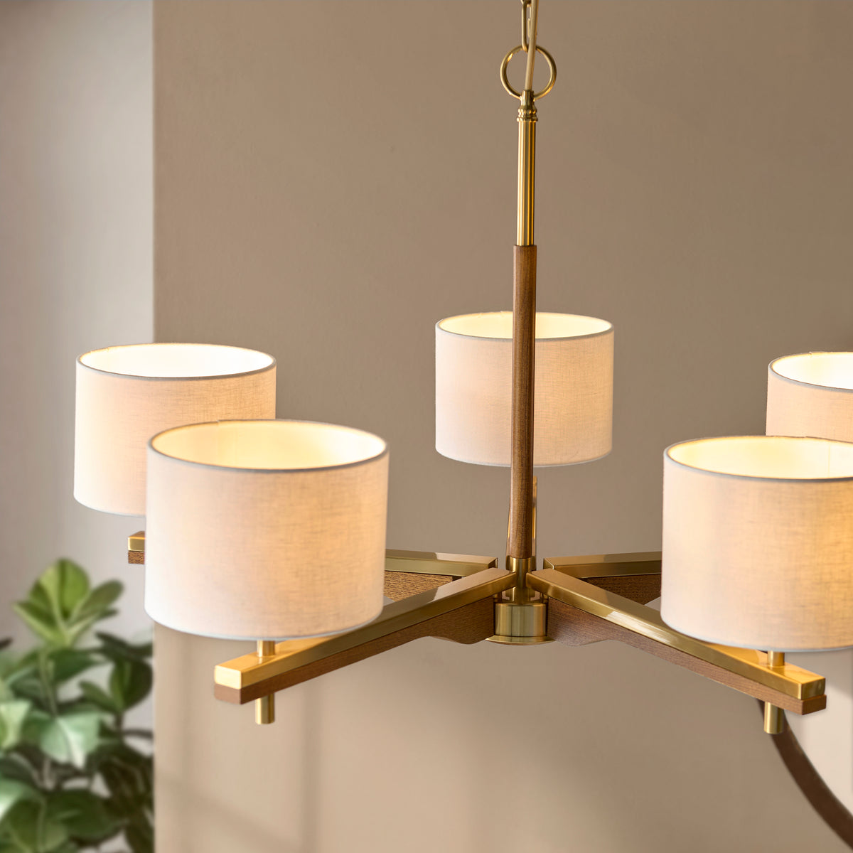 A modern chandelier with five white fabric shades and a brass and wood frame.