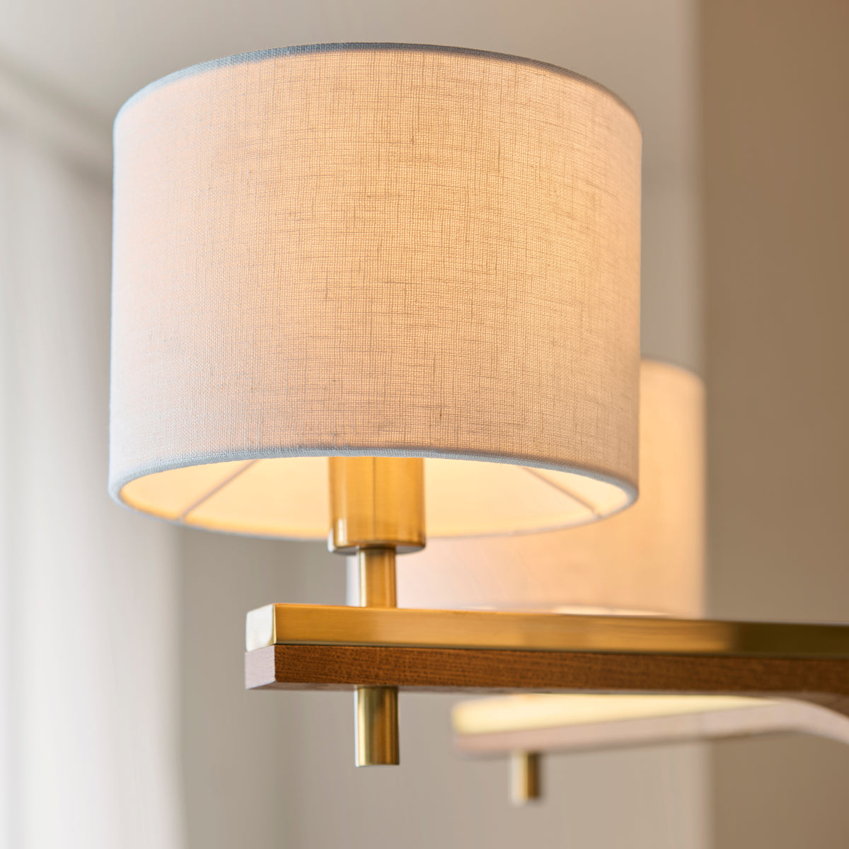 Close-up of a modern chandelier with a light fabric shade and brass accents, emitting a warm glow.