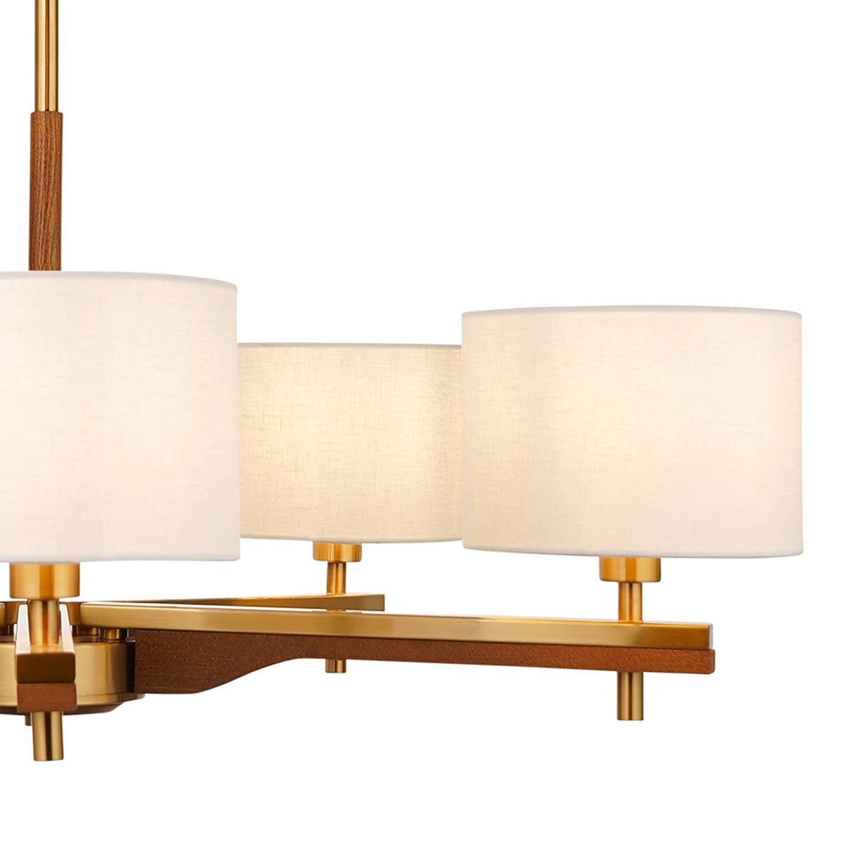 Close-up of a modern chandelier with three cream fabric shades and a wooden and brass frame. 