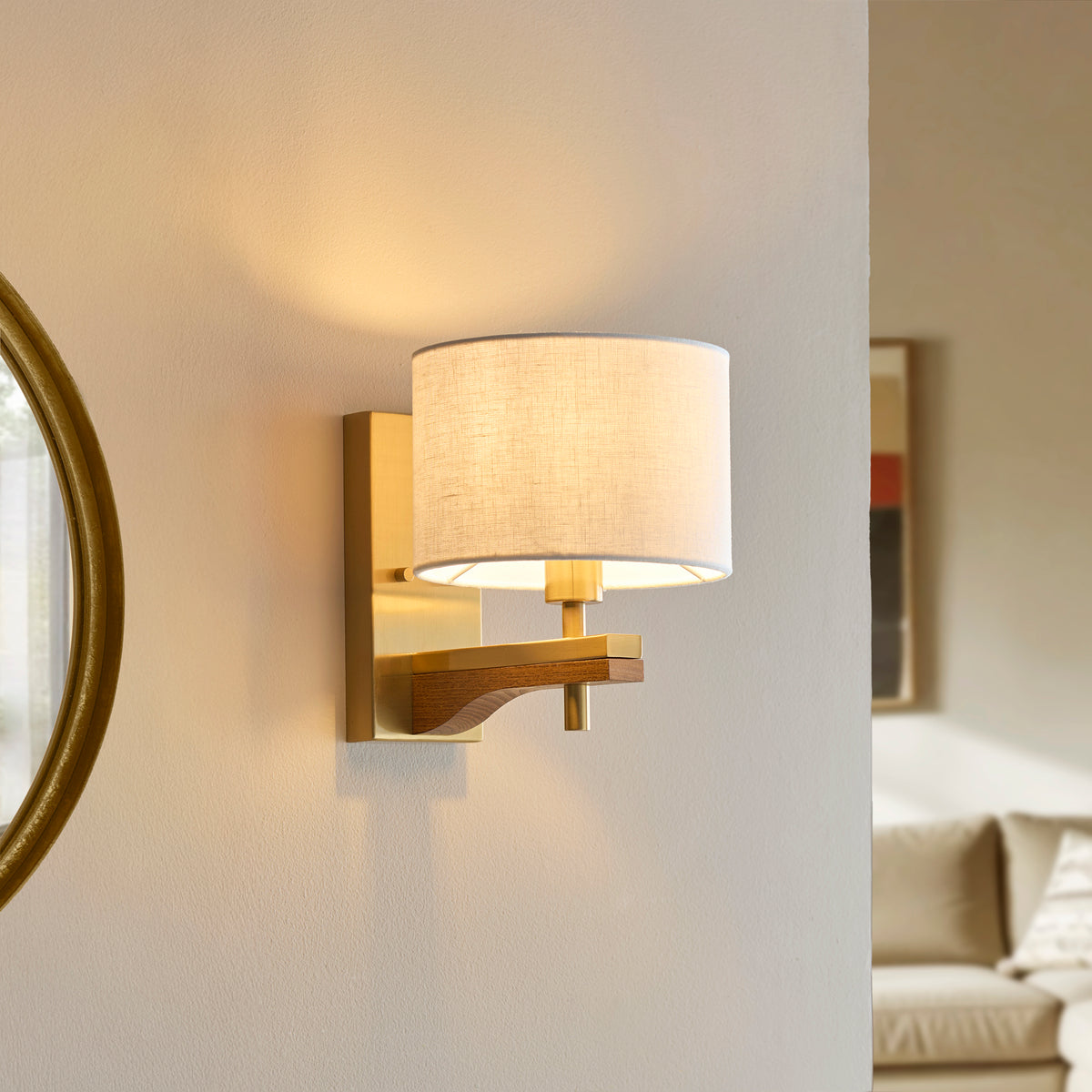 Modern brass wall sconce with a white fabric shade and a wooden accent, illuminating a light-colored wall.