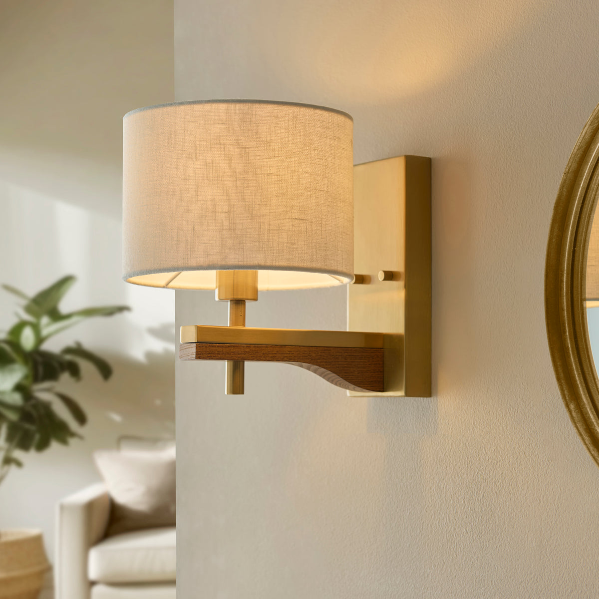 A modern wall sconce with a fabric shade and brass finish, casting a warm glow on a light-colored wall.