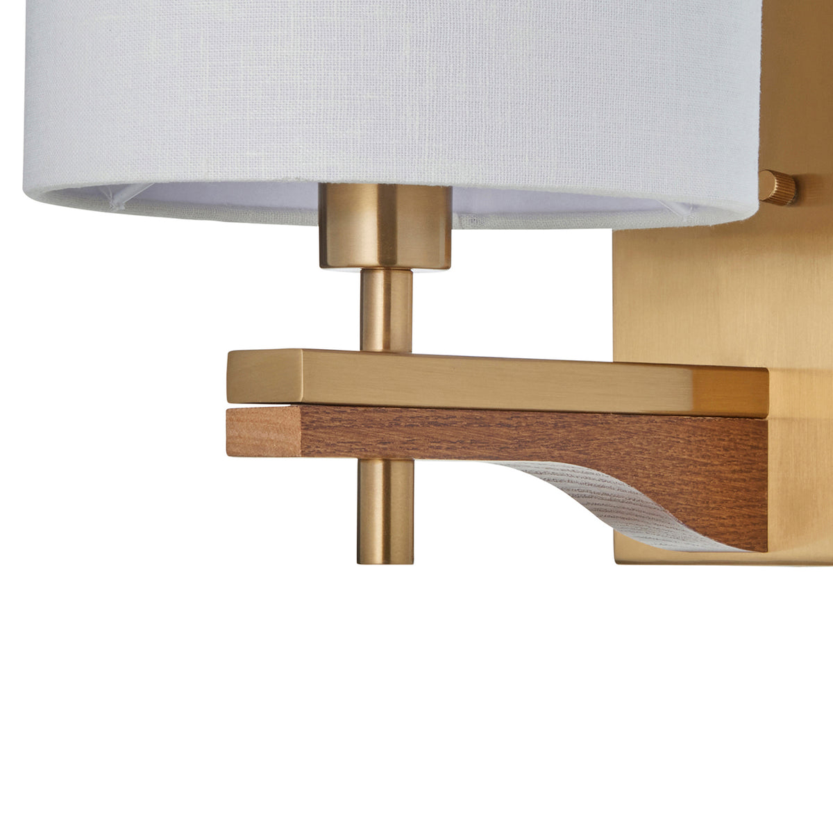 Close-up of a wall sconce with a white fabric shade, brushed brass accents, and a curved wooden detail.