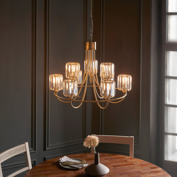 A gold chandelier with crystal shades hangs over a wooden dining table set for dinner.