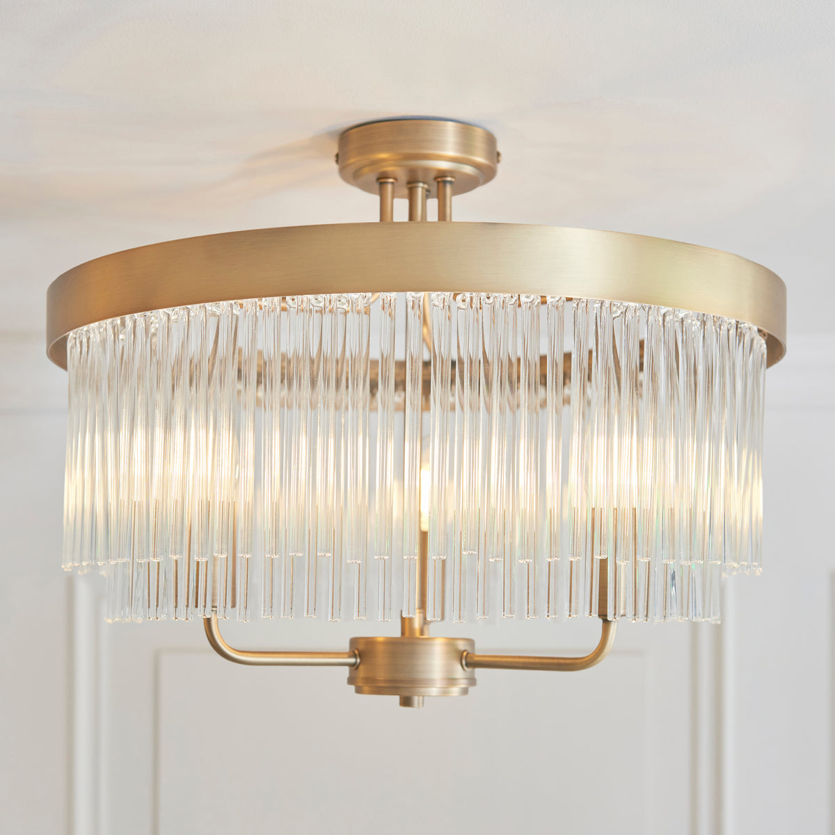 A close-up of a brass ceiling light with a cylindrical shade made of clear glass rods, illuminated.