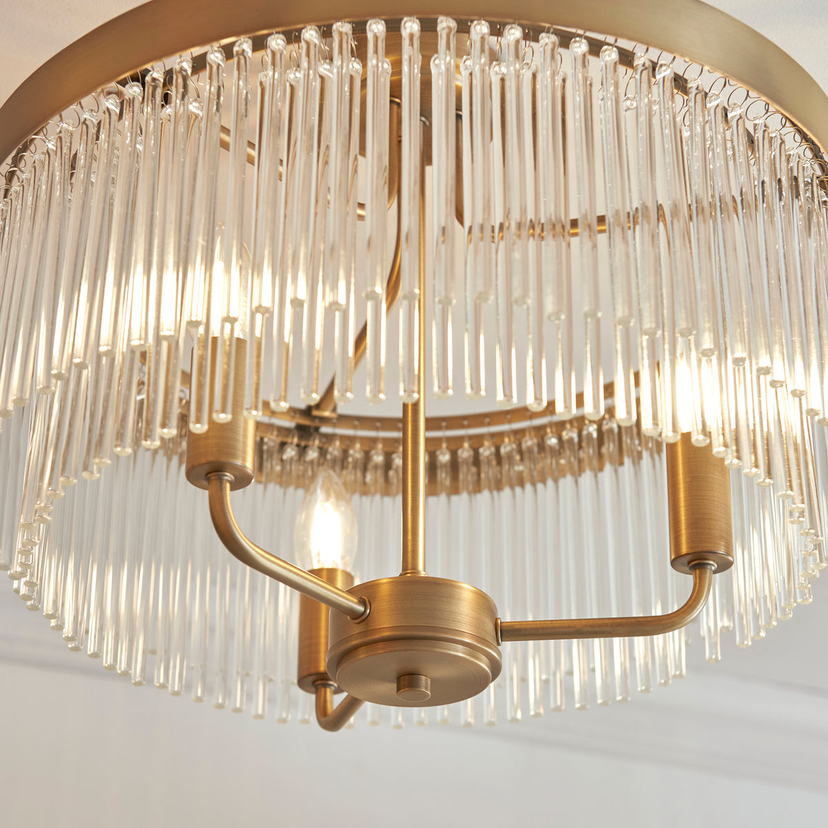 Close-up of a brass chandelier with clear glass rods, illuminated by three glowing bulbs.