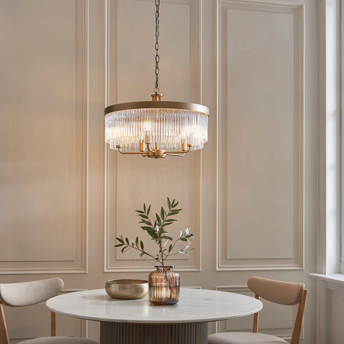 A gold chandelier with clear glass rods hangs above a round marble table with two chairs.