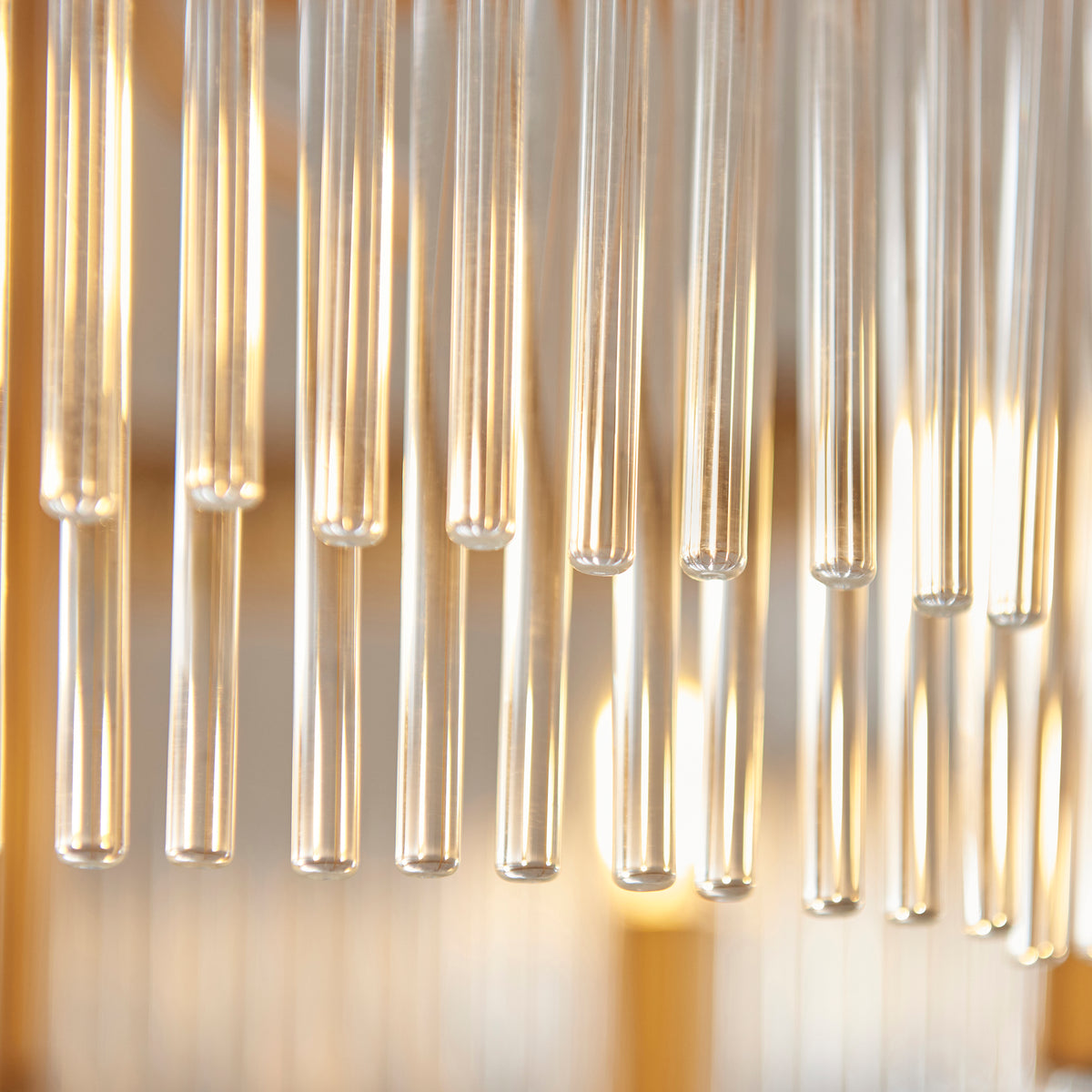 Close-up of clear glass tubes hanging, reflecting warm light from behind, creating vertical streaks of brightness.
