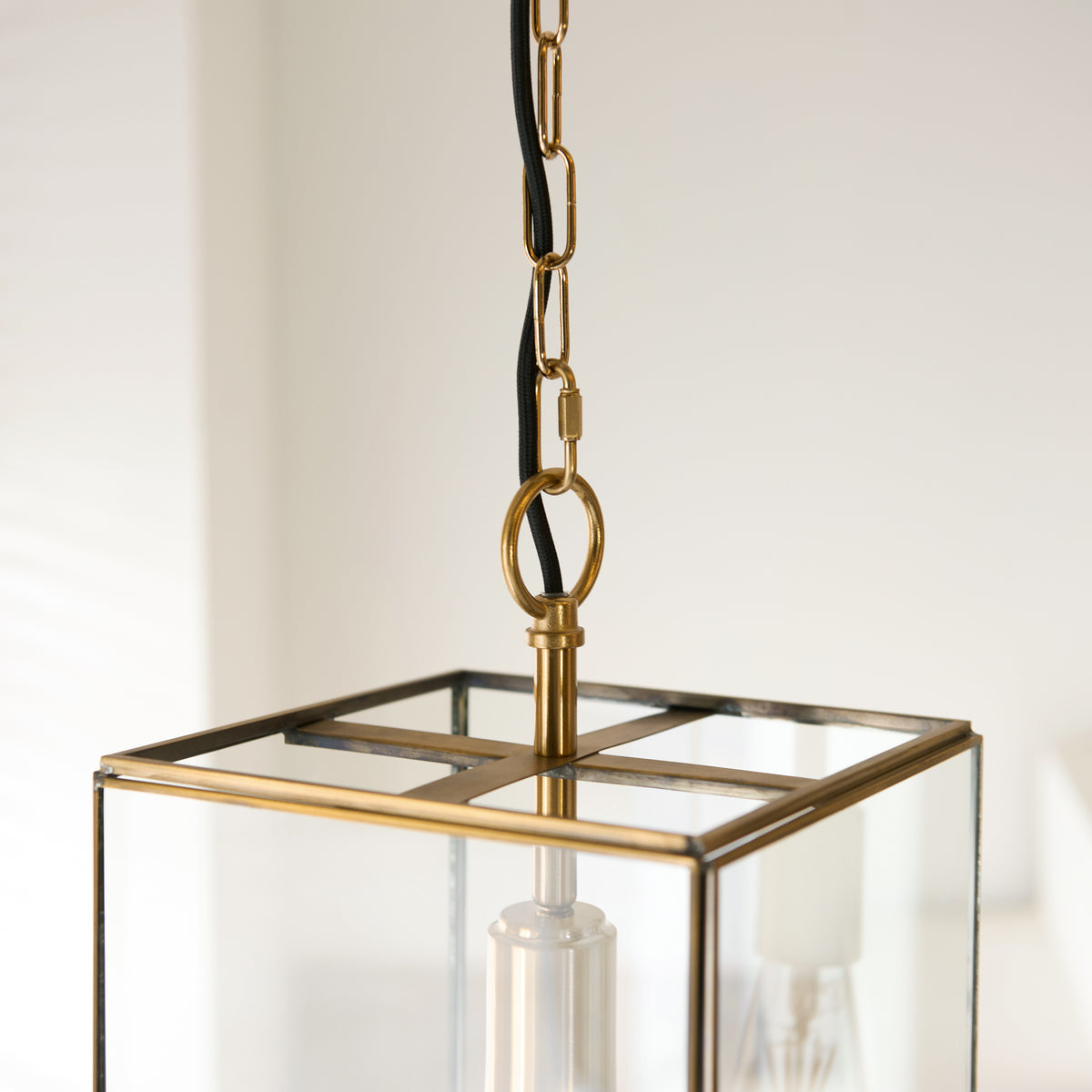 Close-up of a brass and glass lantern pendant light with a black cord and chain.