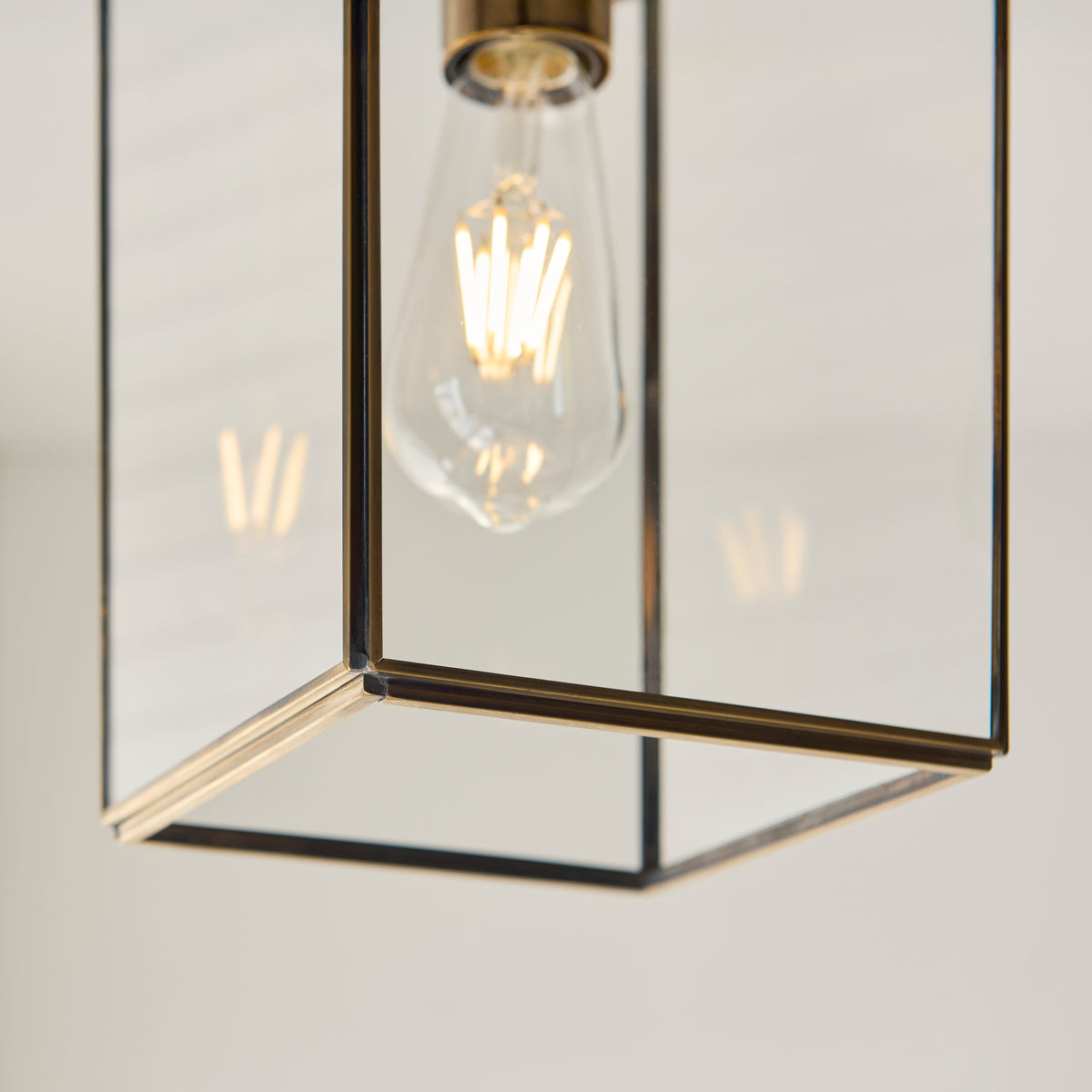 Close-up of a modern brass and glass pendant light with an exposed filament bulb.