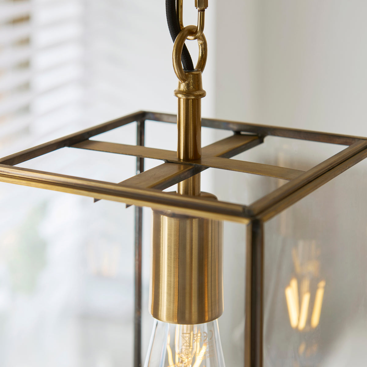 Close-up of a brass lantern pendant light with a visible filament bulb.