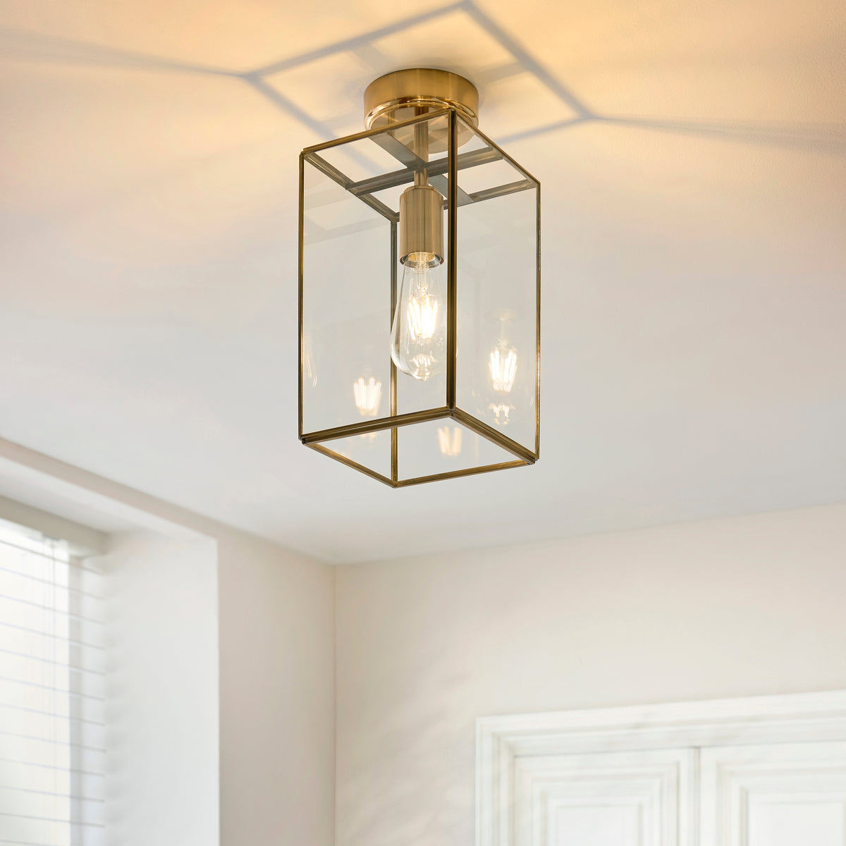 A brass and glass flush mount ceiling light with an exposed Edison bulb, casting geometric shadows.