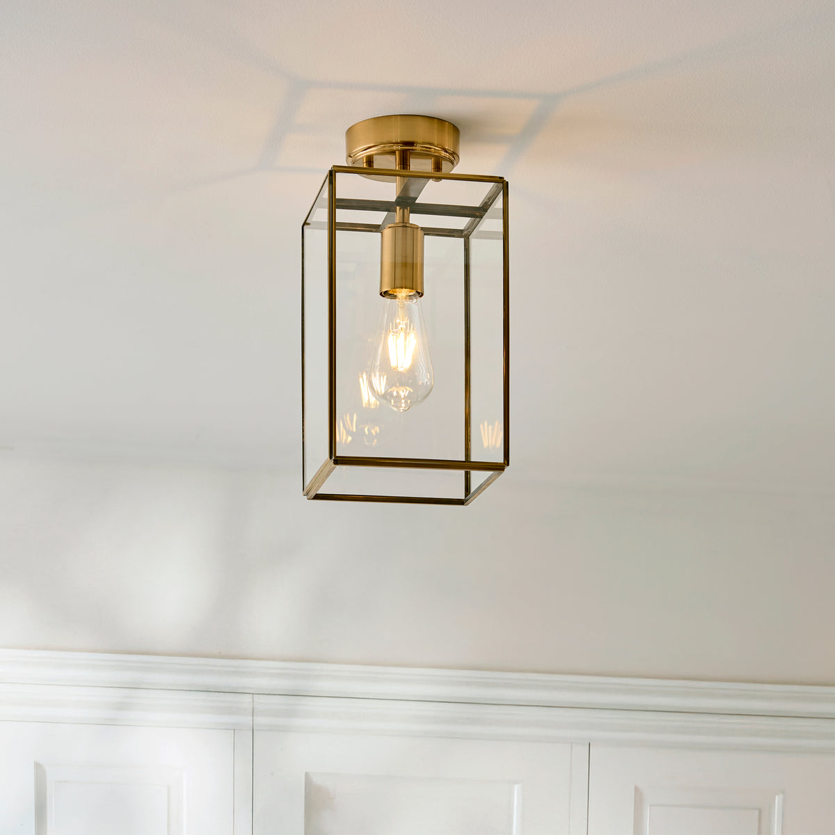 A brass and glass flush mount ceiling light with an exposed Edison bulb.