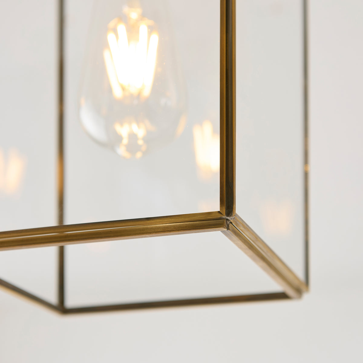Close-up of a clear glass and brass lantern pendant light with a glowing filament bulb inside.