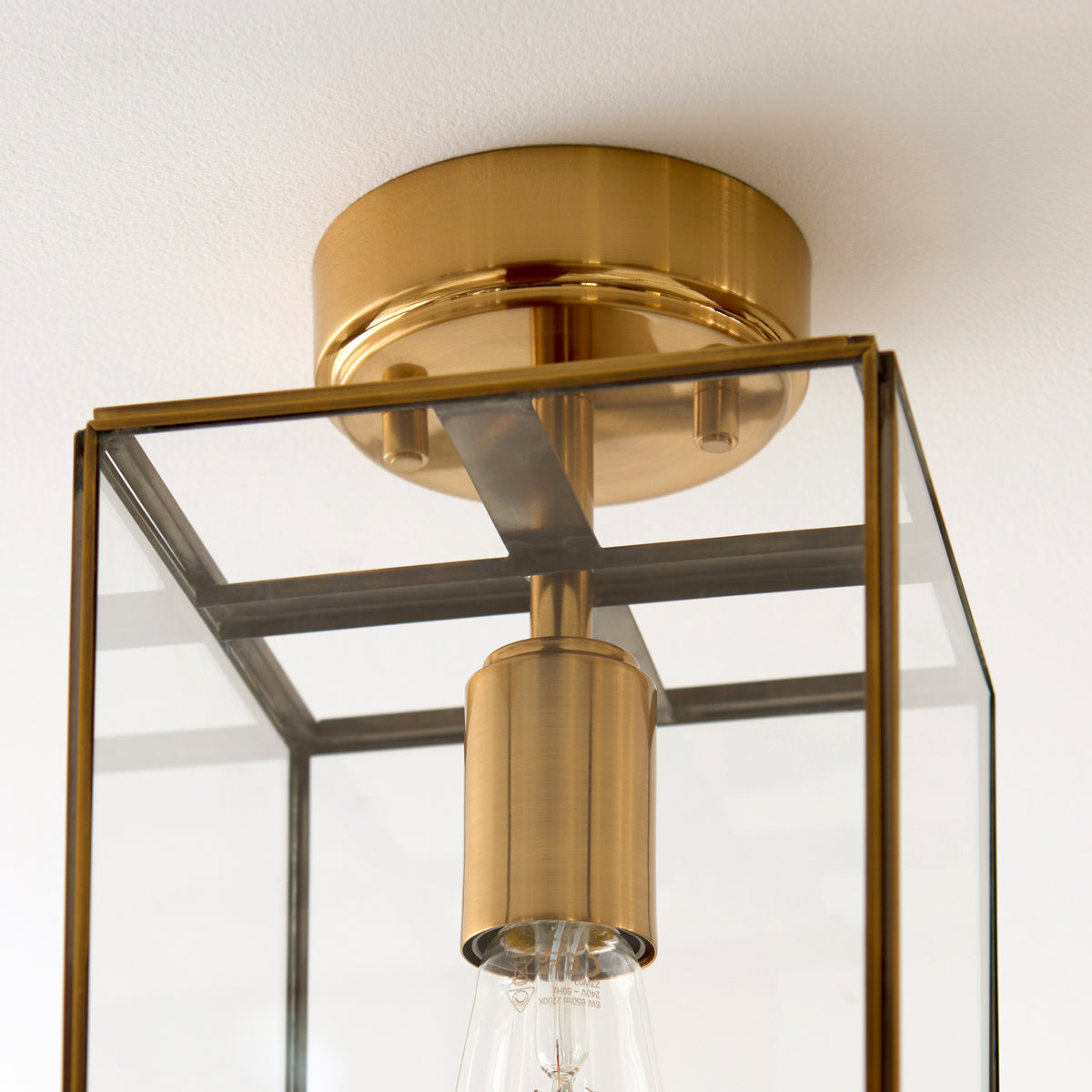 Close-up of a brass and glass flush mount ceiling light with an exposed bulb.