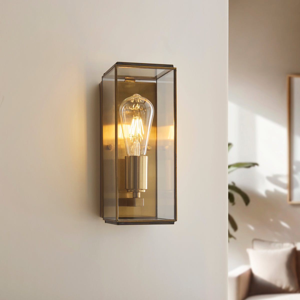 A brass and glass wall sconce with an exposed Edison bulb illuminates a light-colored wall.