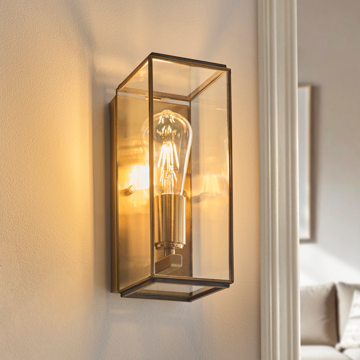 A rectangular wall sconce with a clear glass shade and an exposed filament bulb, casting a warm glow.