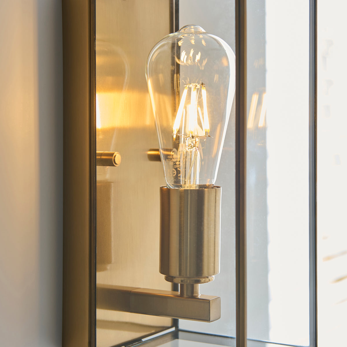 Close-up of a brass wall sconce with a clear, glowing LED filament bulb.