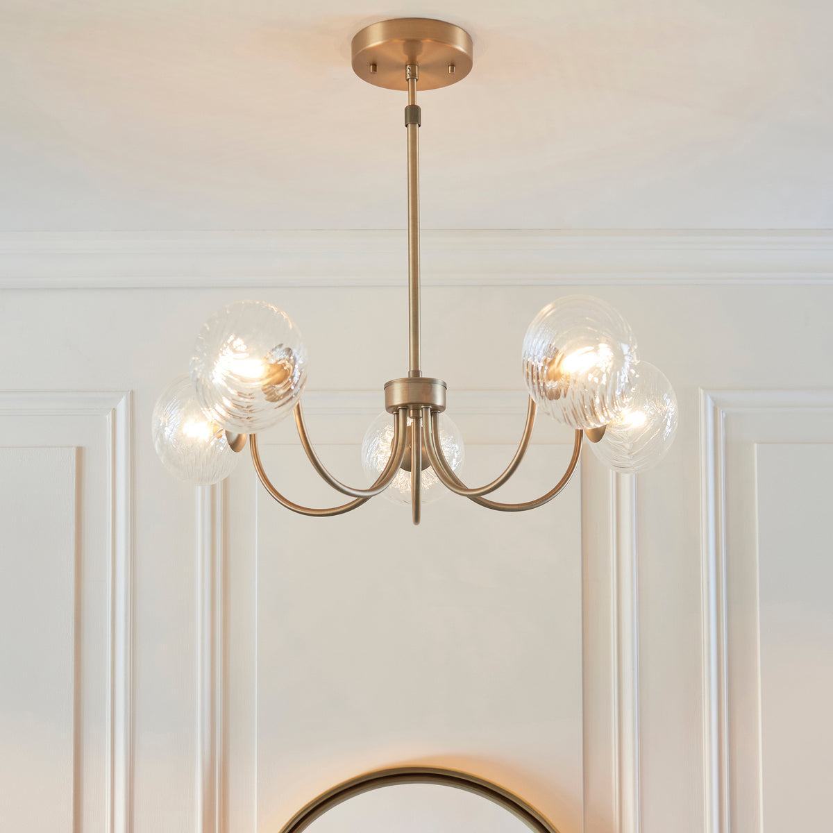 A gold chandelier with five clear, textured glass globes hangs from a white ceiling.