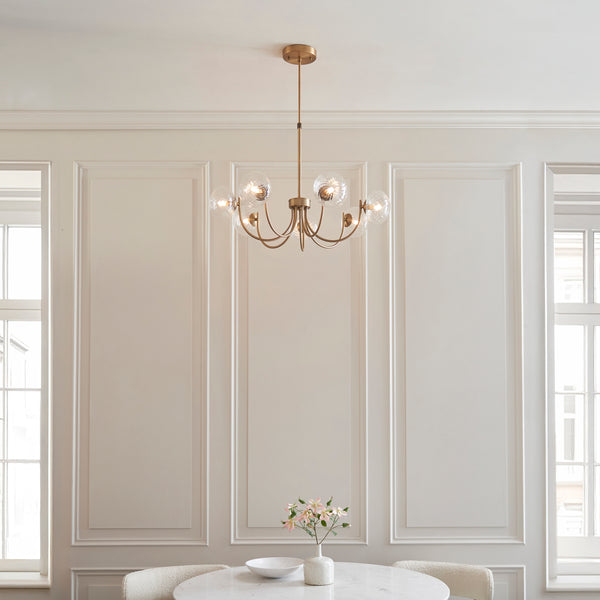 A gold chandelier with clear glass globes hangs above a white marble table with a vase of pink flowers.