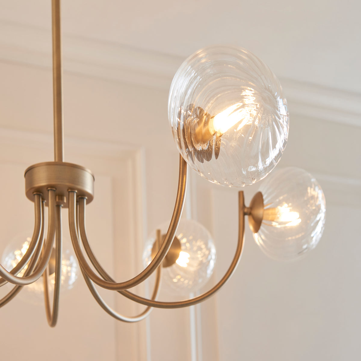 Close-up of a gold chandelier with five clear, textured glass globes, each containing an illuminated bulb.