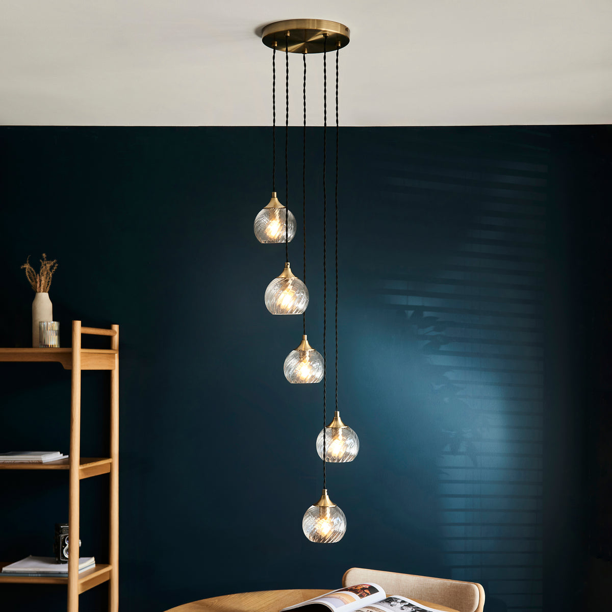 Five glass pendant lights with brass accents hang from the ceiling, illuminating a dark blue wall.
