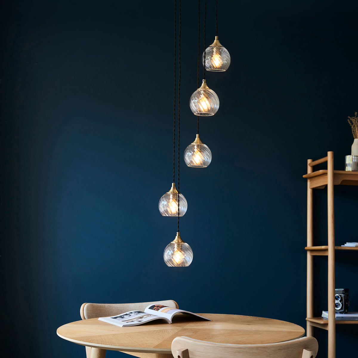 Five glass pendant lights with brass fittings hang above a wooden dining table and chairs.