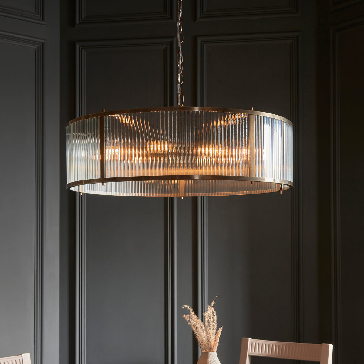 A large, round chandelier with a fluted glass shade and brass frame hangs above a dining table.