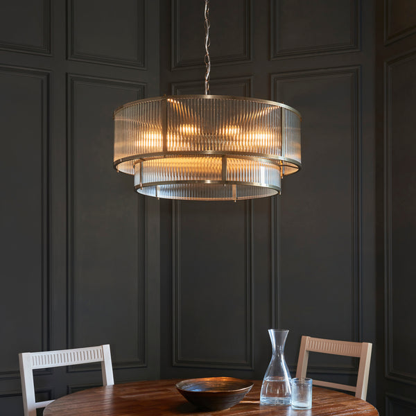 A large, two-tiered chandelier with fluted glass shades and a brass frame hangs over a wooden dining table.