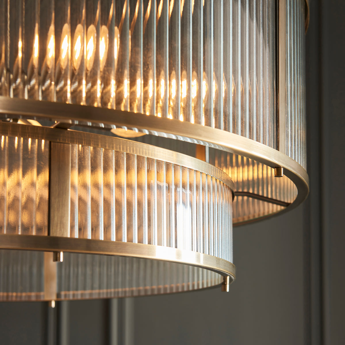 Close-up of a tiered chandelier with fluted glass and antique brass accents, glowing warmly.