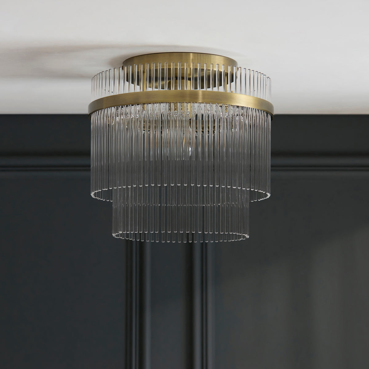 A close-up of a brass and glass ceiling light fixture with two tiers of glass rods.