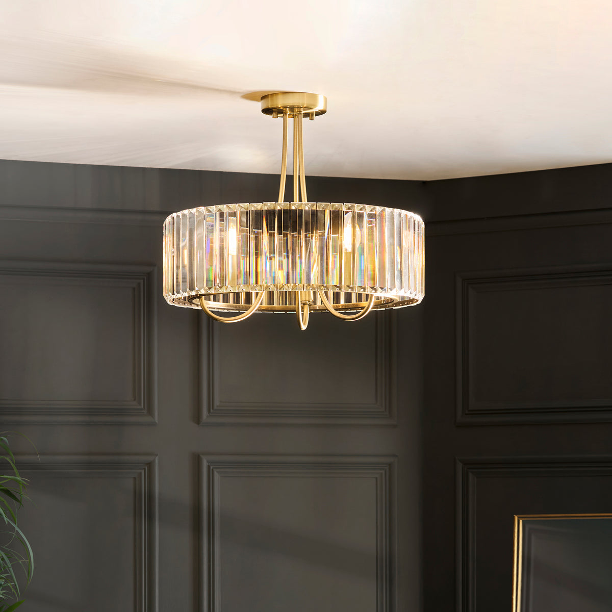 A gold and crystal chandelier hangs from a white ceiling, illuminating a dark paneled wall.