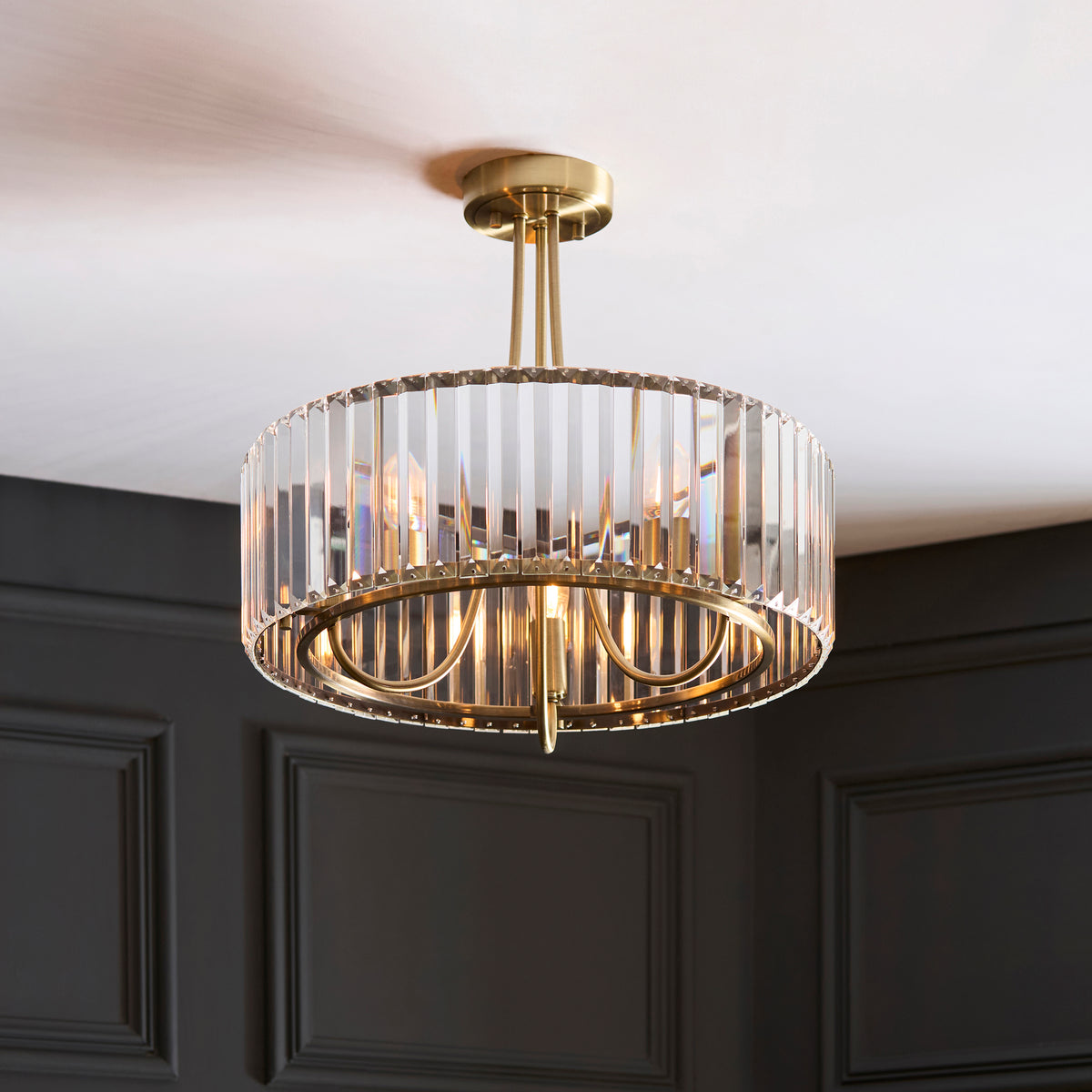 A brass and crystal chandelier hangs from a white ceiling, illuminating a dark paneled wall.