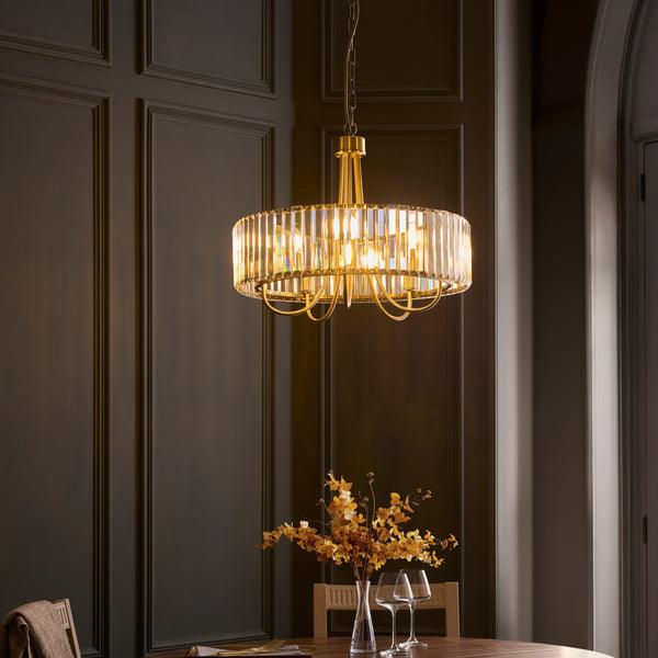 A gold and crystal chandelier hangs above a dining table with a vase of dried flowers and wine glasses.
