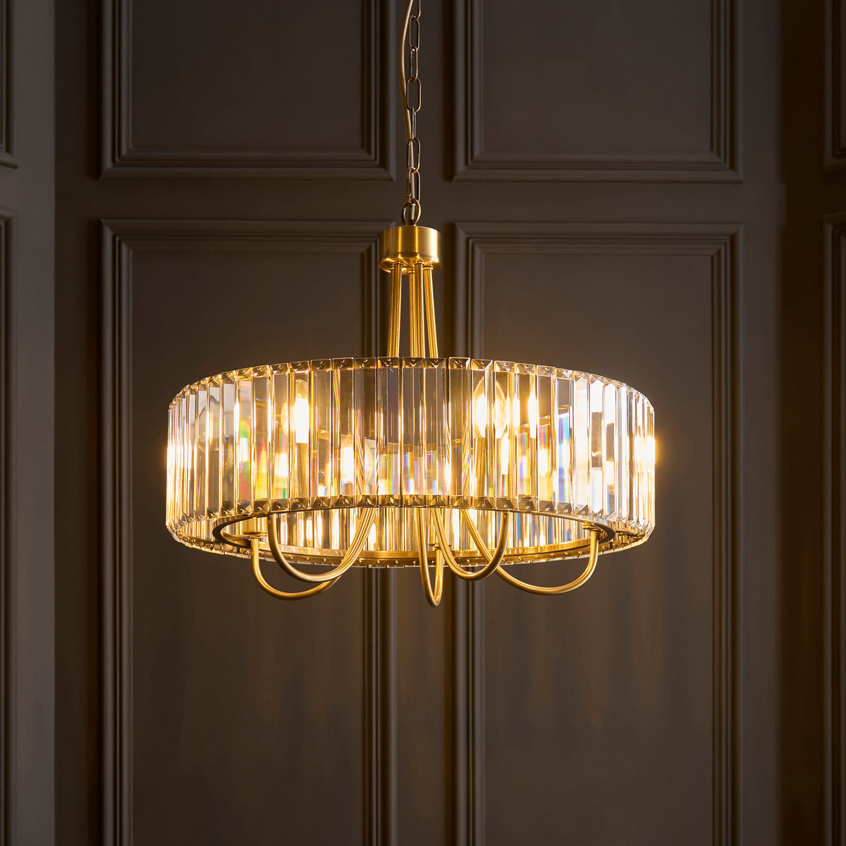 A gold chandelier with a crystal-encrusted drum shade hangs against a dark paneled wall.