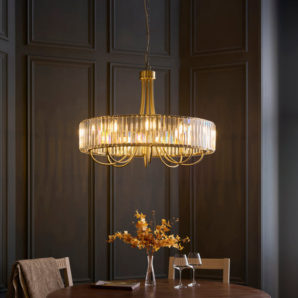 A gold chandelier with a crystal-encrusted drum shade hangs above a dining table with a vase of dried flowers.