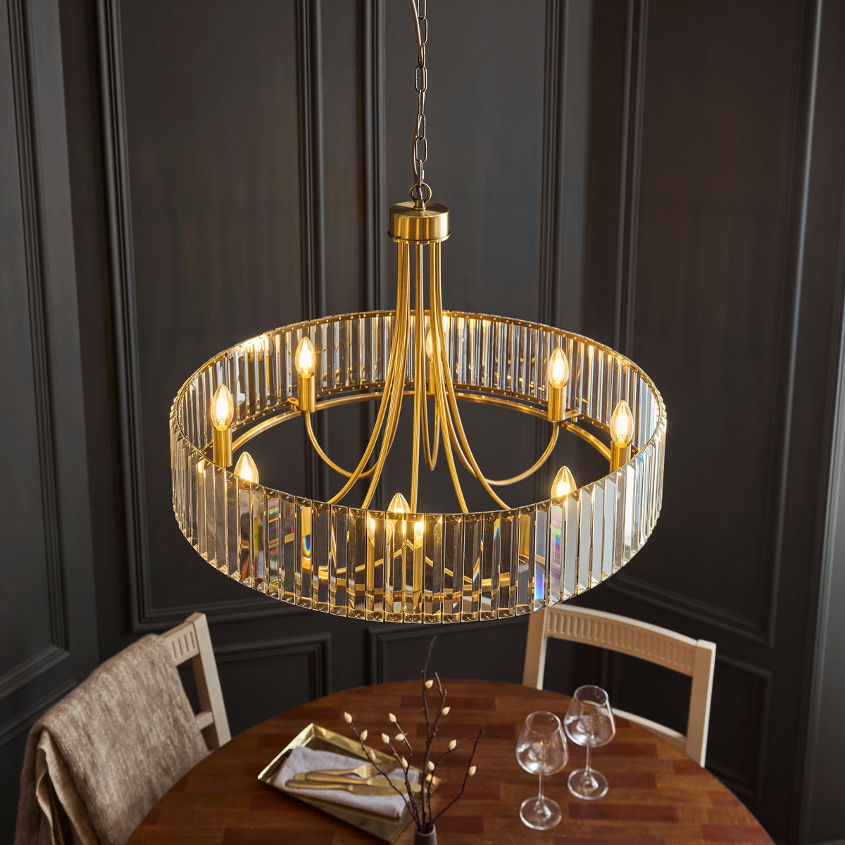 A gold chandelier with crystal accents hangs above a wooden dining table set with glasses and cutlery.