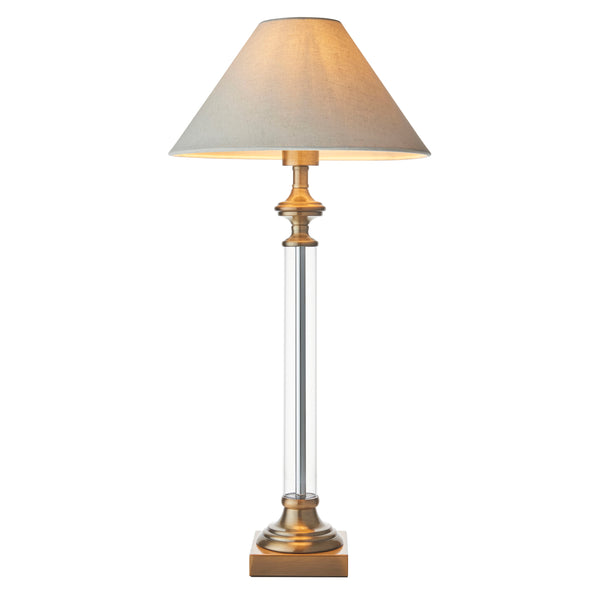 Elegant table lamp with a beige fabric shade, clear glass column, and antique brass base.