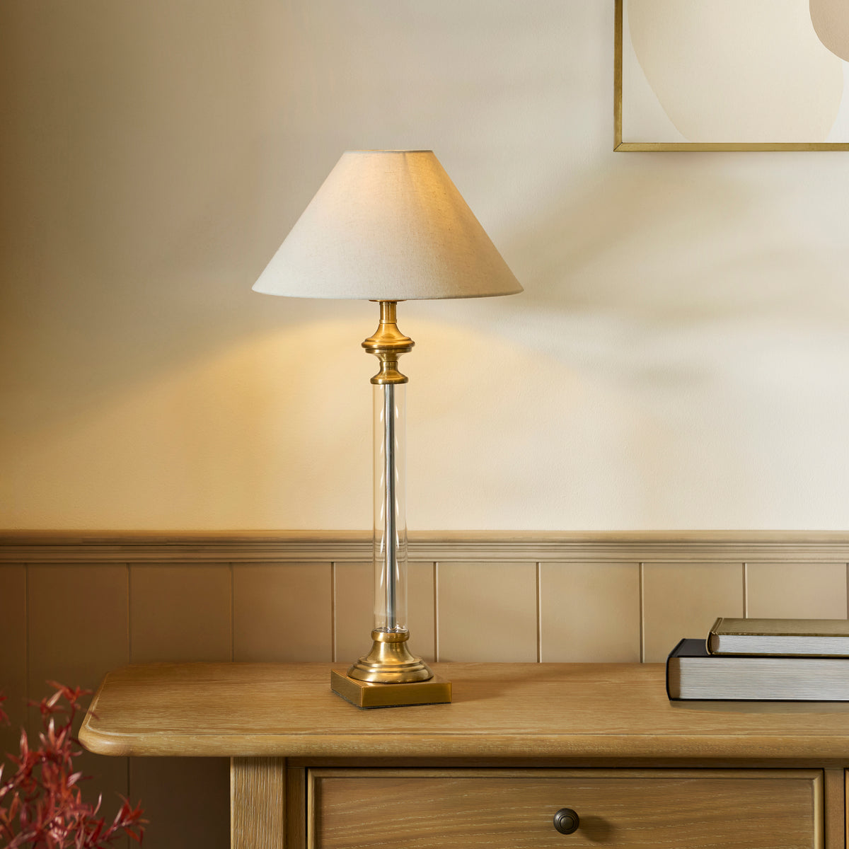 A brass and glass table lamp with a white shade sits on a wooden table with books.