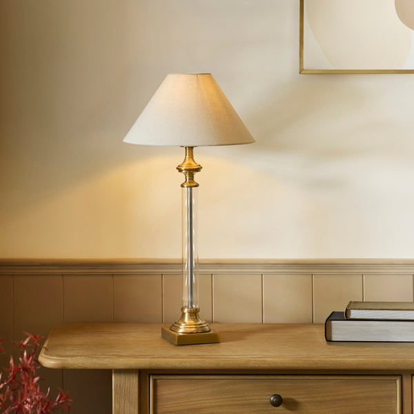 A brass and glass table lamp with a white shade sits on a wooden table with books.