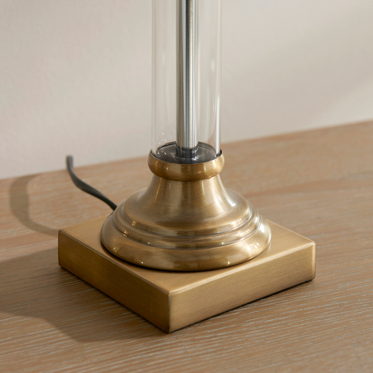 Close-up of a table lamp base, featuring a square antique brass base and a round, fluted brass column.