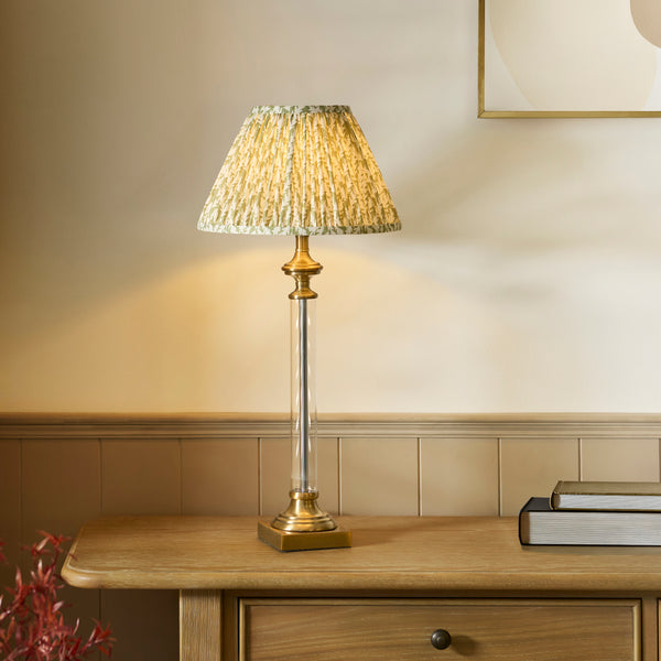 A tall table lamp with a pleated green and yellow lampshade sits on a wooden console table.