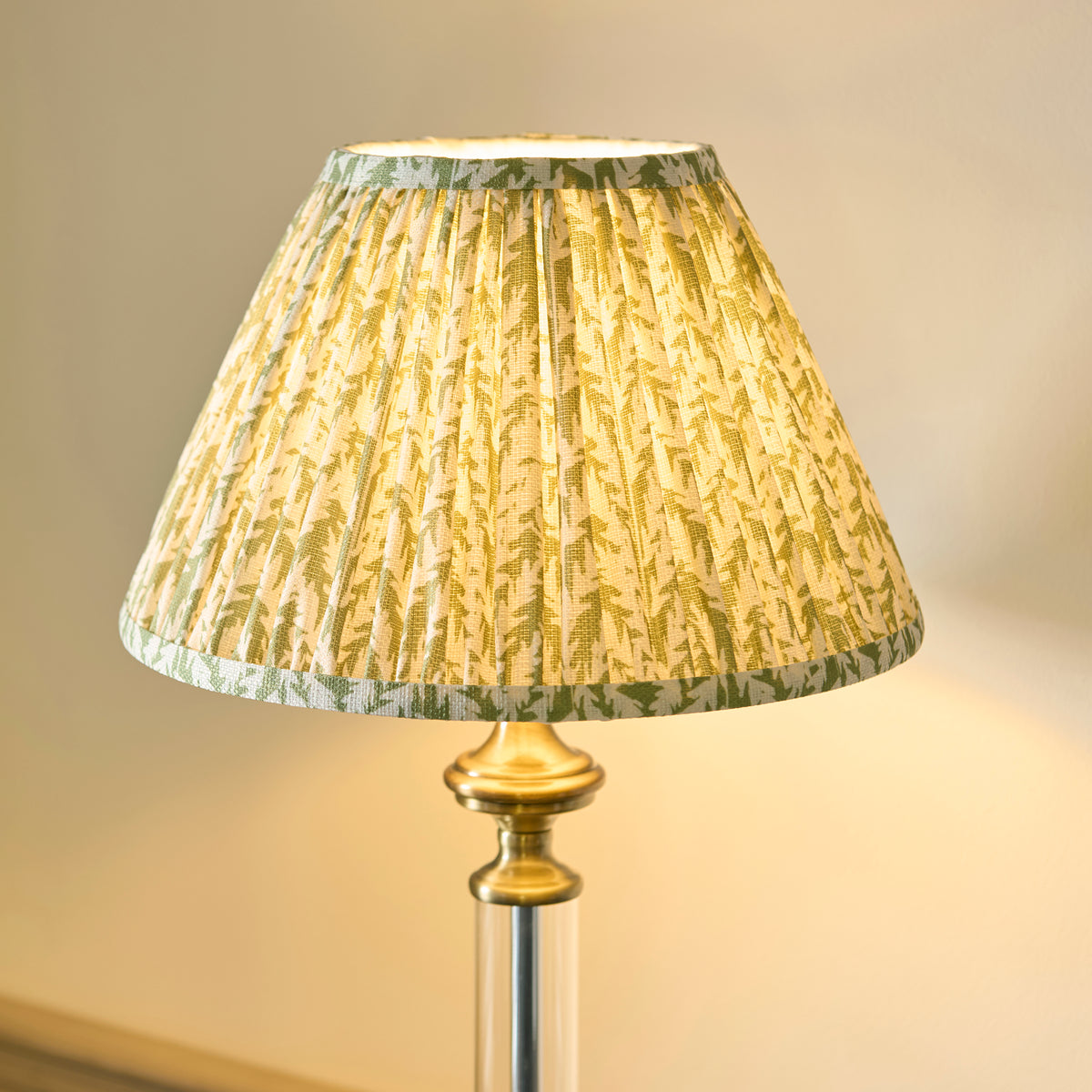 Table lamp with a pleated, patterned shade in green and yellow, casting a warm glow.