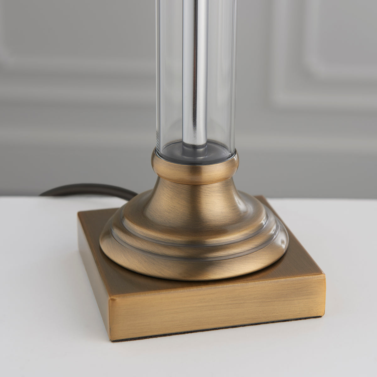 Close-up of a lamp base with a square antique brass base and a round, fluted antique brass column.